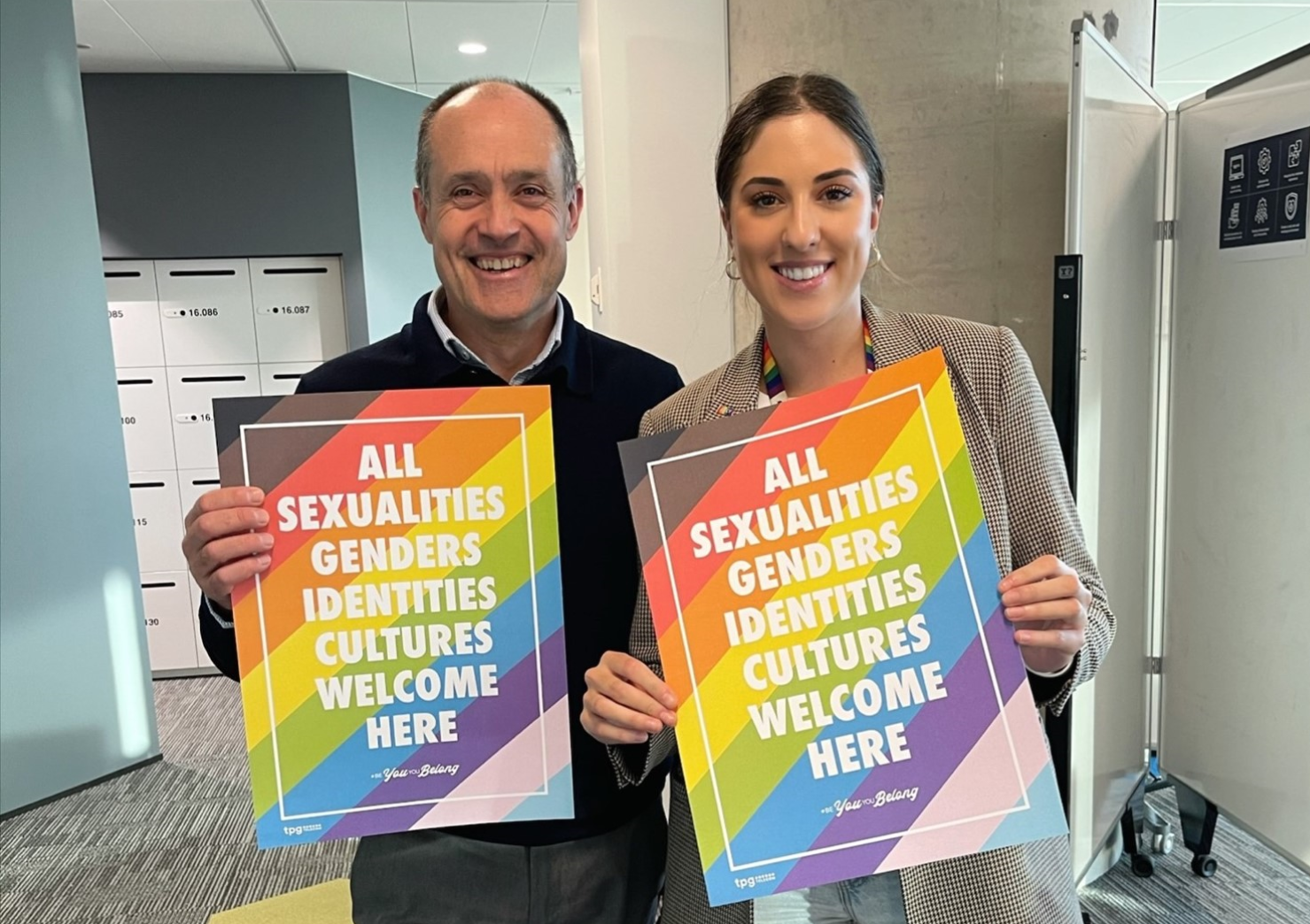 Two persons, smiling and holding a poster related to diversity and inclusion, stand next to each other.